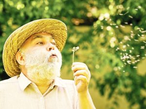 Photo of man in a hat blowing a dandelion, metaphorically representing memories during alzheimer's