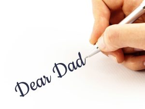 Photo of a hand holding a pen, writing Dear Dad.