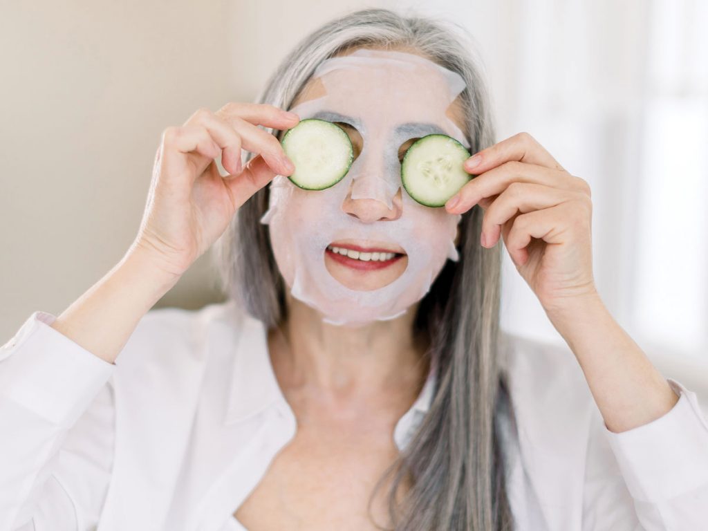 Photo of senior woman doing a skin cleanse, holding up cucumber slices to her eyes