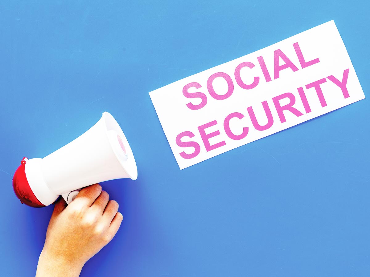 Senior activist conceptual photo of a hand holding a bullhorn pointed at a sign that reads "SOCIAL SECURITY" on a blue background.