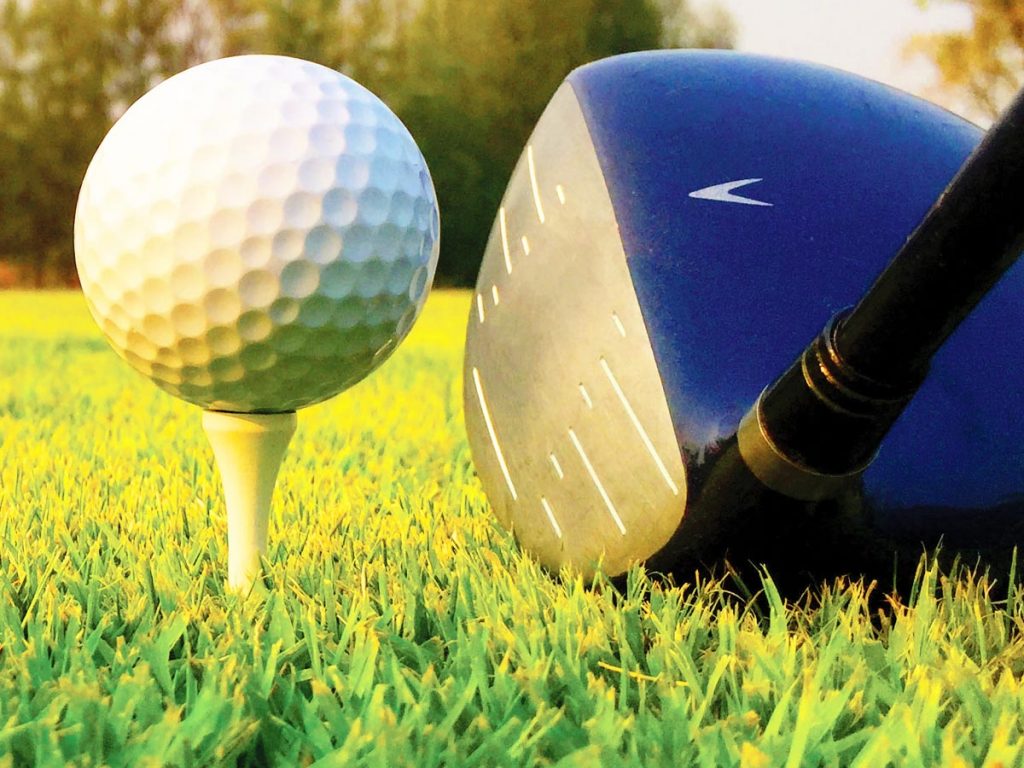 Closeup photo of a driver aiming at a golf ball resting on a tee.