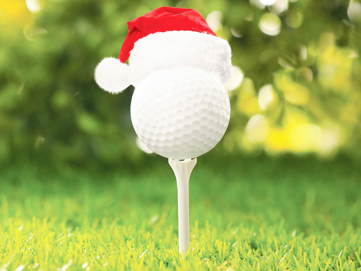 Closeup photo of a tee'd up golf ball sporting a Santa hat.