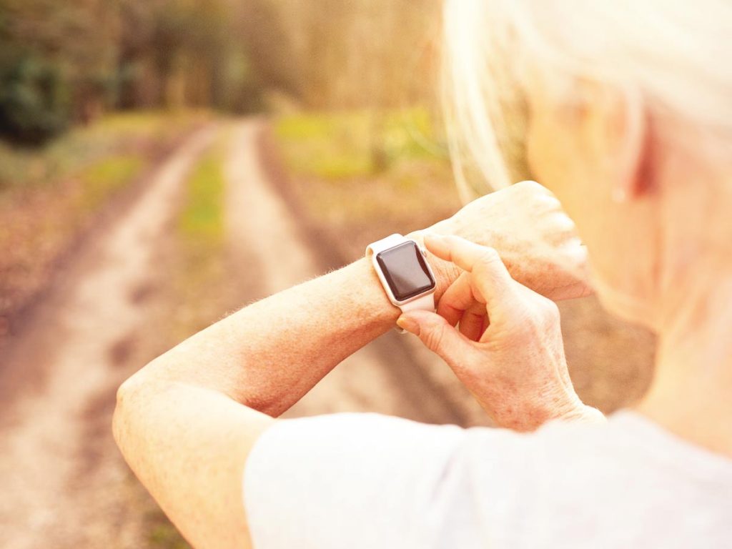 photo of a senior woman checking her fitness watch before running a rutted dirt road