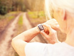 photo of a senior woman checking her fitness watch before running a rutted dirt road