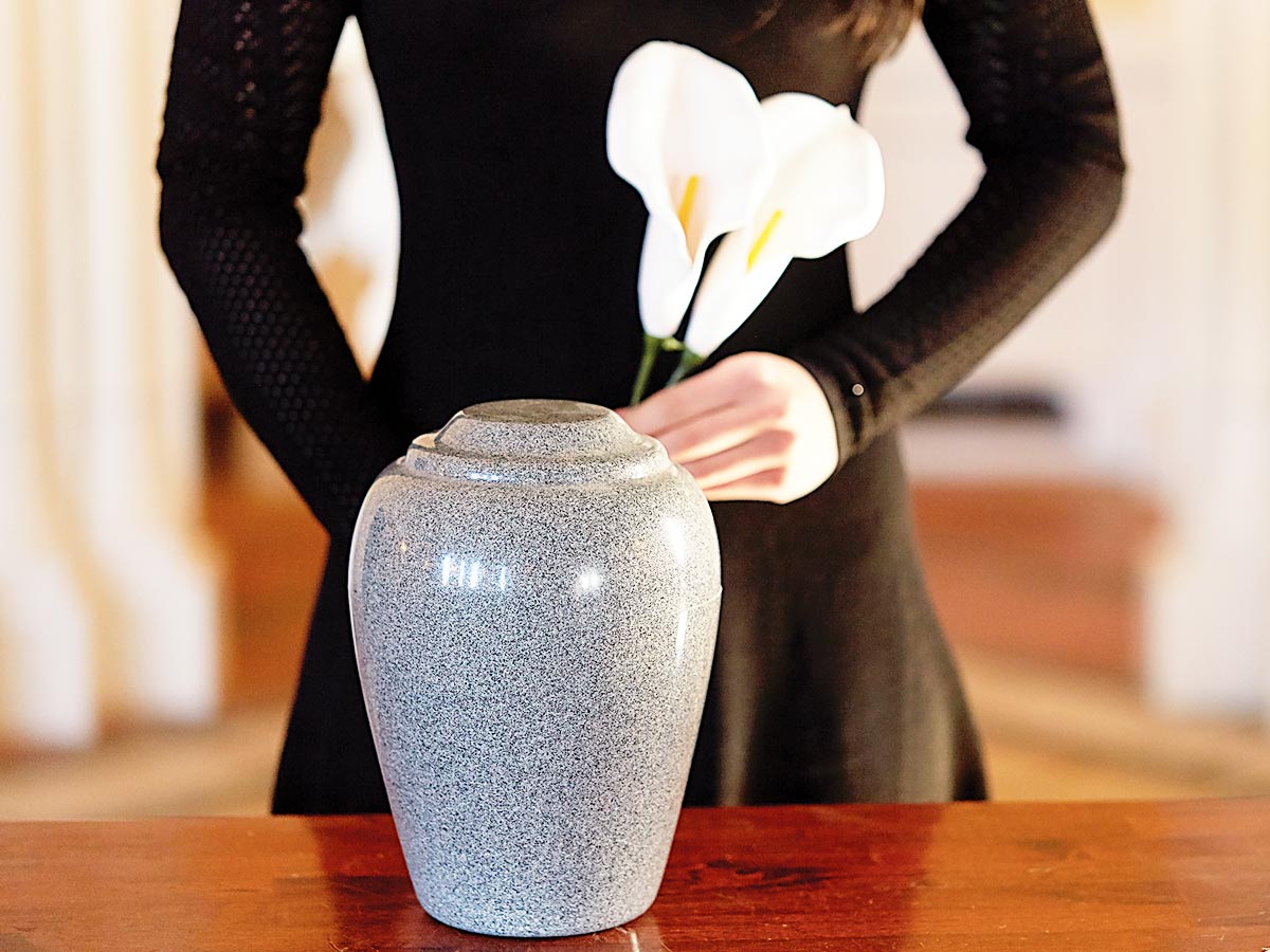 cropped image of woman in black dress, holding an iris, while standing behind an urn