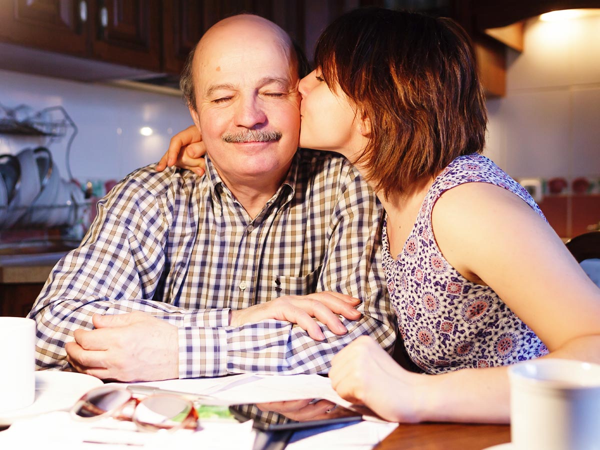 Woman kissing her father's cheek while helping him with his finances
