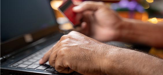 Closeup photo of hands entering a credit card number into the computer, representing the concept of exposing oneself to cyber threats