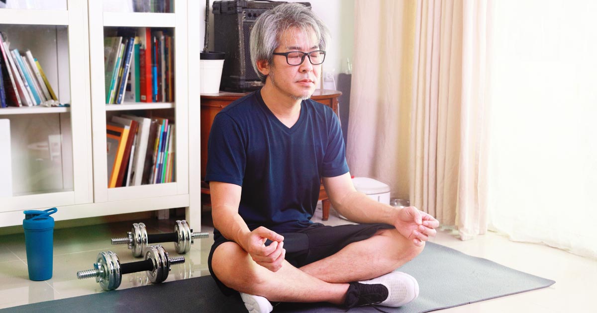 Man seated in a yoga position on a yoga mat, meditating
