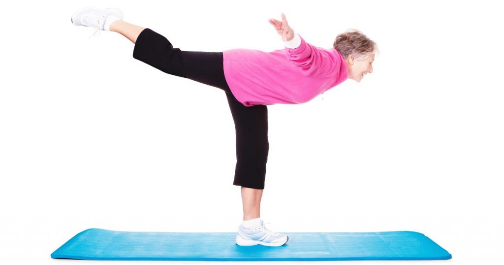 Photo of senior woman balancing on one foot on a yoga mat.
