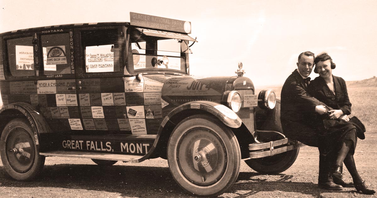 A 1923 Cross-Country Road Trip historic photo of two people from the 20s leaning against the front bumper of a car