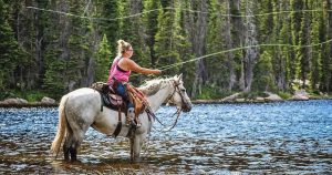 Photo of a woman in a river fishing on horseback