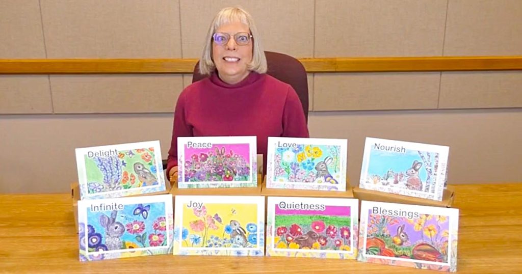 Photo of music therapist Barbara Zuck sitting behind a table that has a display of her AtoZ Activity Cards for helping people with memory issues.