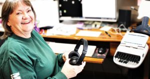 Deanne Tweeter sitting at her desk in her home office, holding a headphone set
